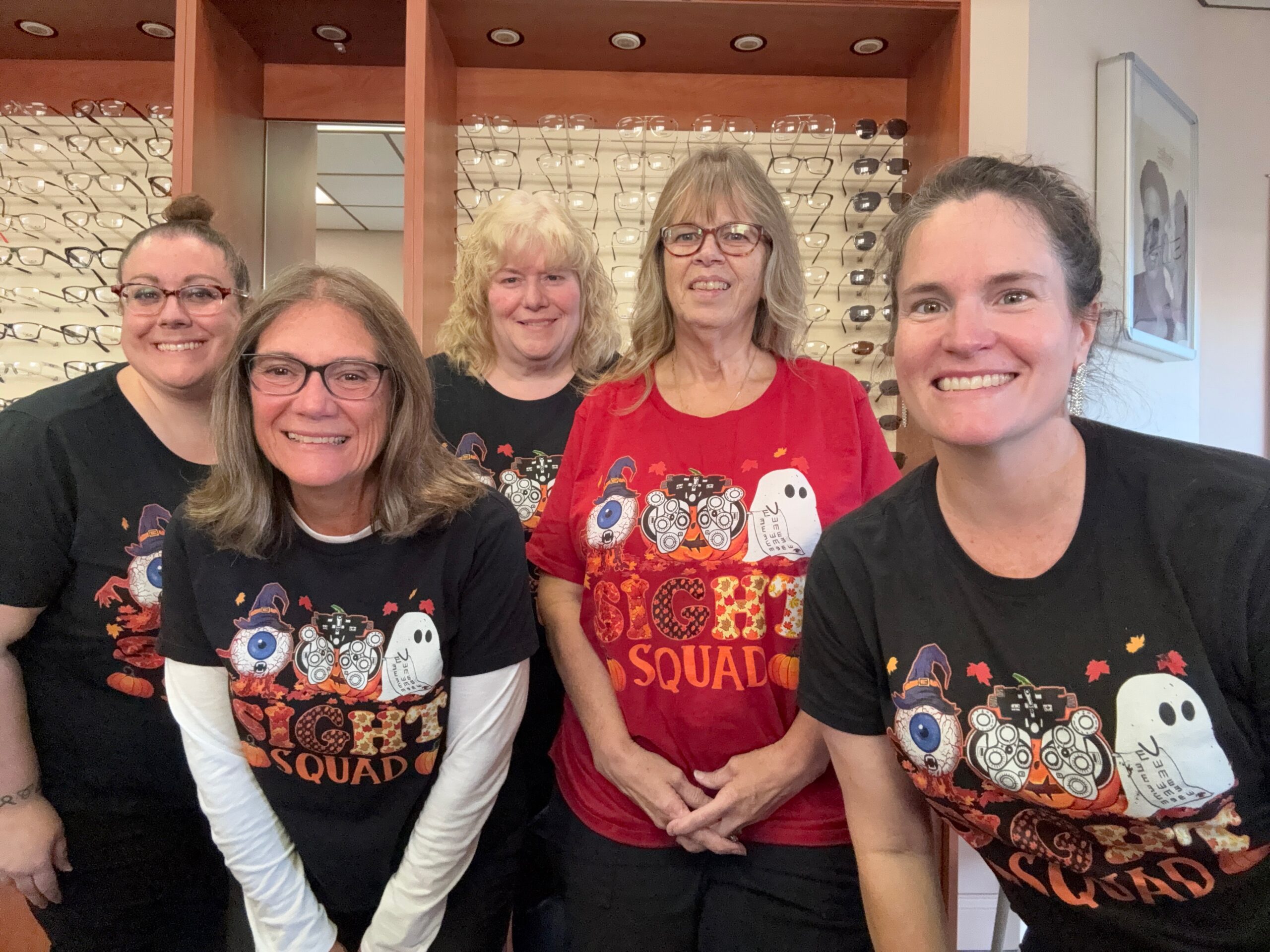 IMG_8502 Five caucasian women wearing Halloween shirts with the wording "Sight Squad" . An image of an eyeball wearing a witches hat, a pumpkin looking through a phoropter and a white ghost holding an eyechart is above the wording.